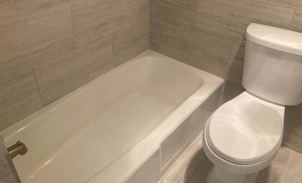 A white bathtub and toilet are installed in a bathroom with beige tile walls and floor.