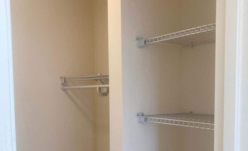 Empty closet with two wire shelves on the right wall and a single hanging rod with a shelf on the left wall.