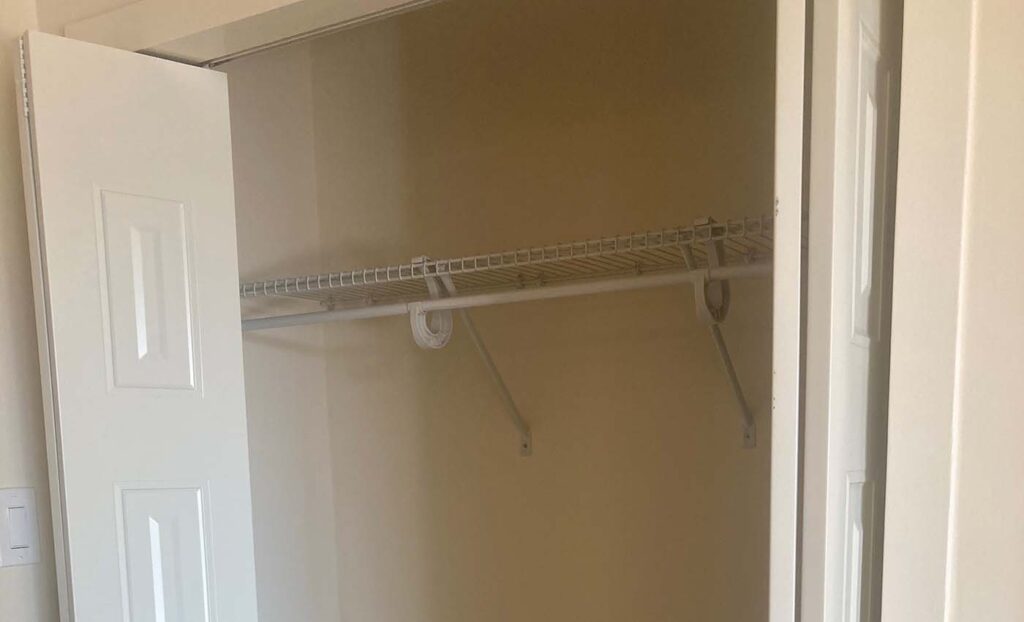 An empty closet with white double doors and a metal wire shelf and hanging rod installed inside.