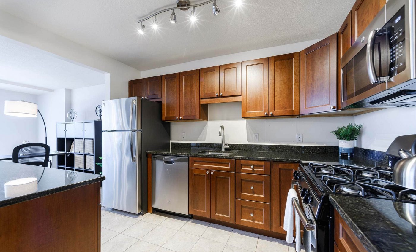 Modern kitchen with wooden cabinets, stainless steel appliances, granite countertops, and tile flooring. A track light fixture is mounted on the ceiling.